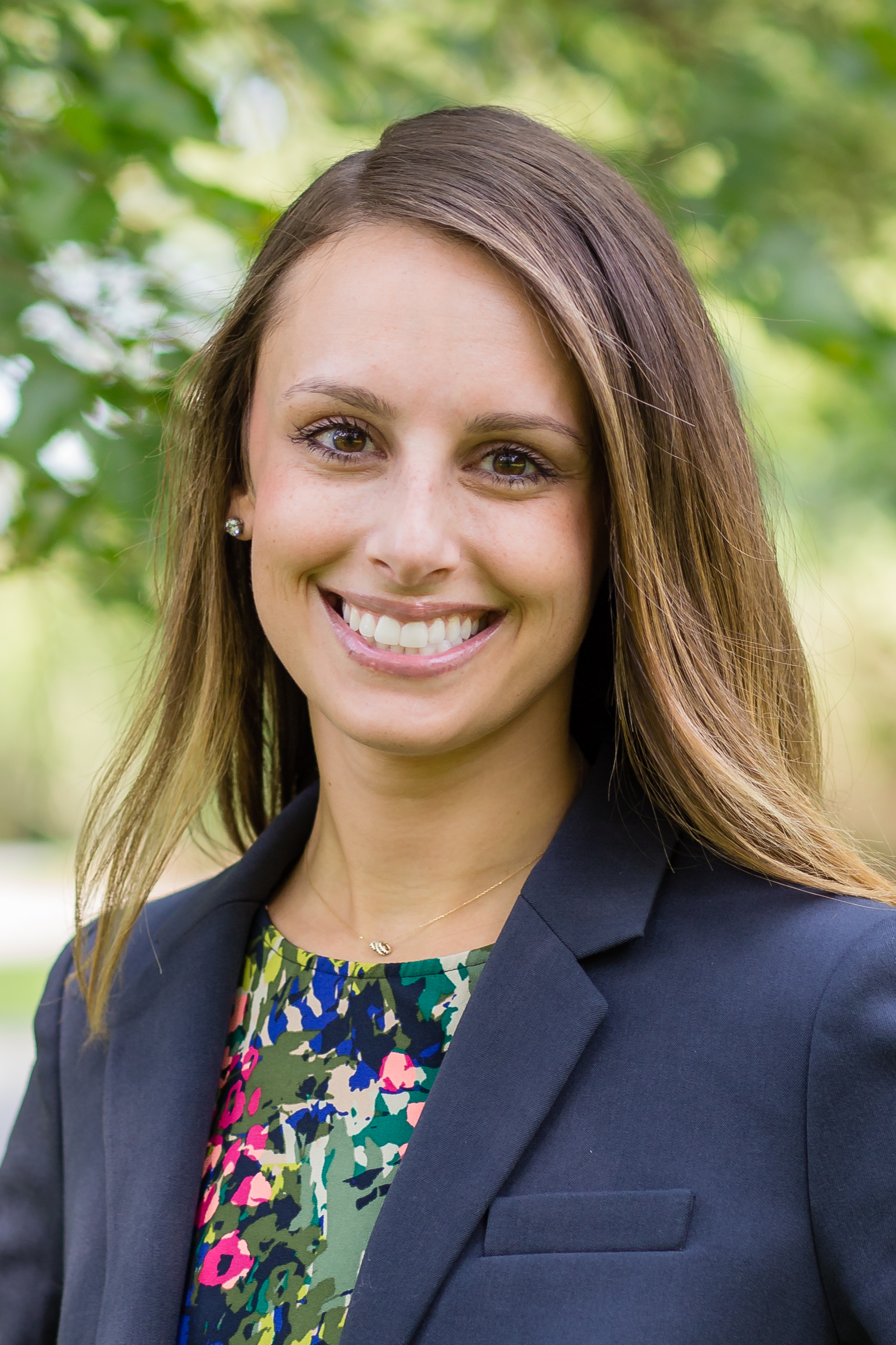 Mandee Heinl smiling in front of a green/leafy background. 