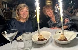Two smiling women sitting at a table with flaming desserts in front of them. 