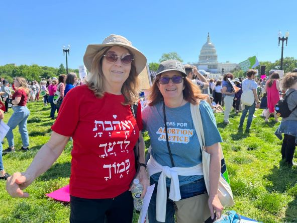 A woman with a red shirt and sun hat standing next to a woman with a blue shirt and a sunhat at a rally. 