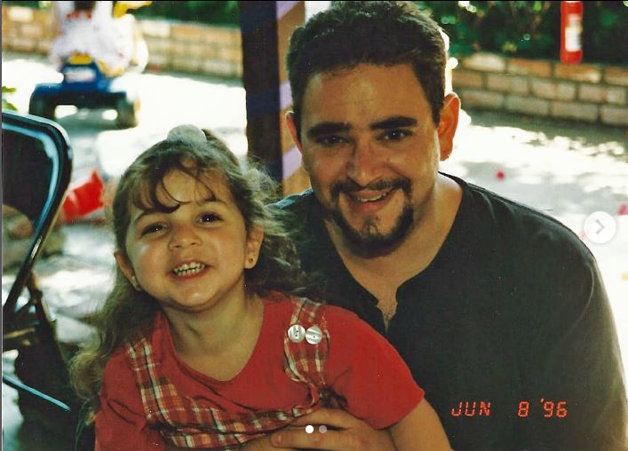 Little girl in a red shirt with older man in darker shirt outside. 